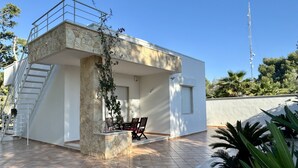 Un edificio moderno con fachada de piedra, un patio cubierto con mesa y sillas, y una escalera que lleva a un nivel superior.