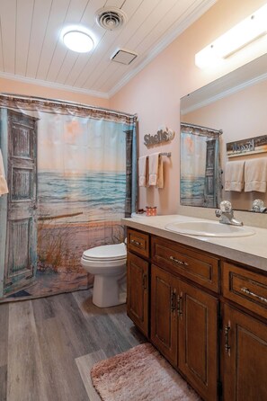 Une salle de bain avec une fresque murale représentant une plage, des meubles en bois, un lavabo et des toilettes.