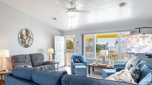 Ein Wohnzimmer mit einem blauen Sofa, einem Sessel, einem Tisch mit Dekoration und einem Deckenventilator, mit Blick ins Freie.