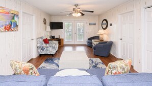 A living room with a ceiling fan, a TV mounted on the wall, and a door leading to an outdoor area. - 3 BR walk to the beach house! Summer House 117    (Garden City)