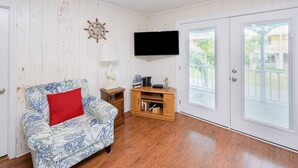 A living room with a floral-patterned sofa, a red cushion, a wooden side table, a flat-screen TV, and a wooden entertainment unit. - 3 BR walk to the beach house! Summer House 117    (Garden City)