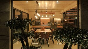 A modern dining area with a wooden table and chairs, a kitchen in the background, and a staircase leading to an upper level.