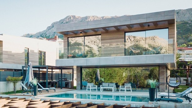 A modern two-story building with a swimming pool, outdoor seating, and mountain views.