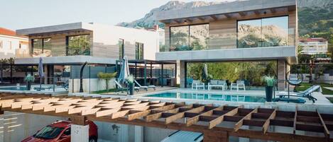 Una villa moderna con piscina, mobiliario exterior y vistas a las montañas.