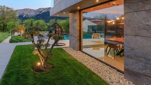 A modern building with a glass entrance, outdoor seating, a small tree, and a pool.