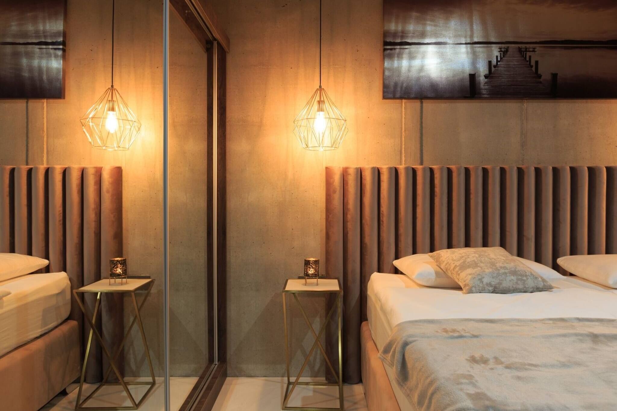 Une chambre d’hôtel moderne avec un grand lit, deux tables de chevet, un miroir et des luminaires suspendus.