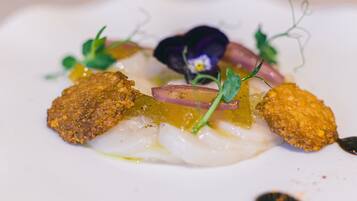A dish with white fish, green herbs, and a purple flower.