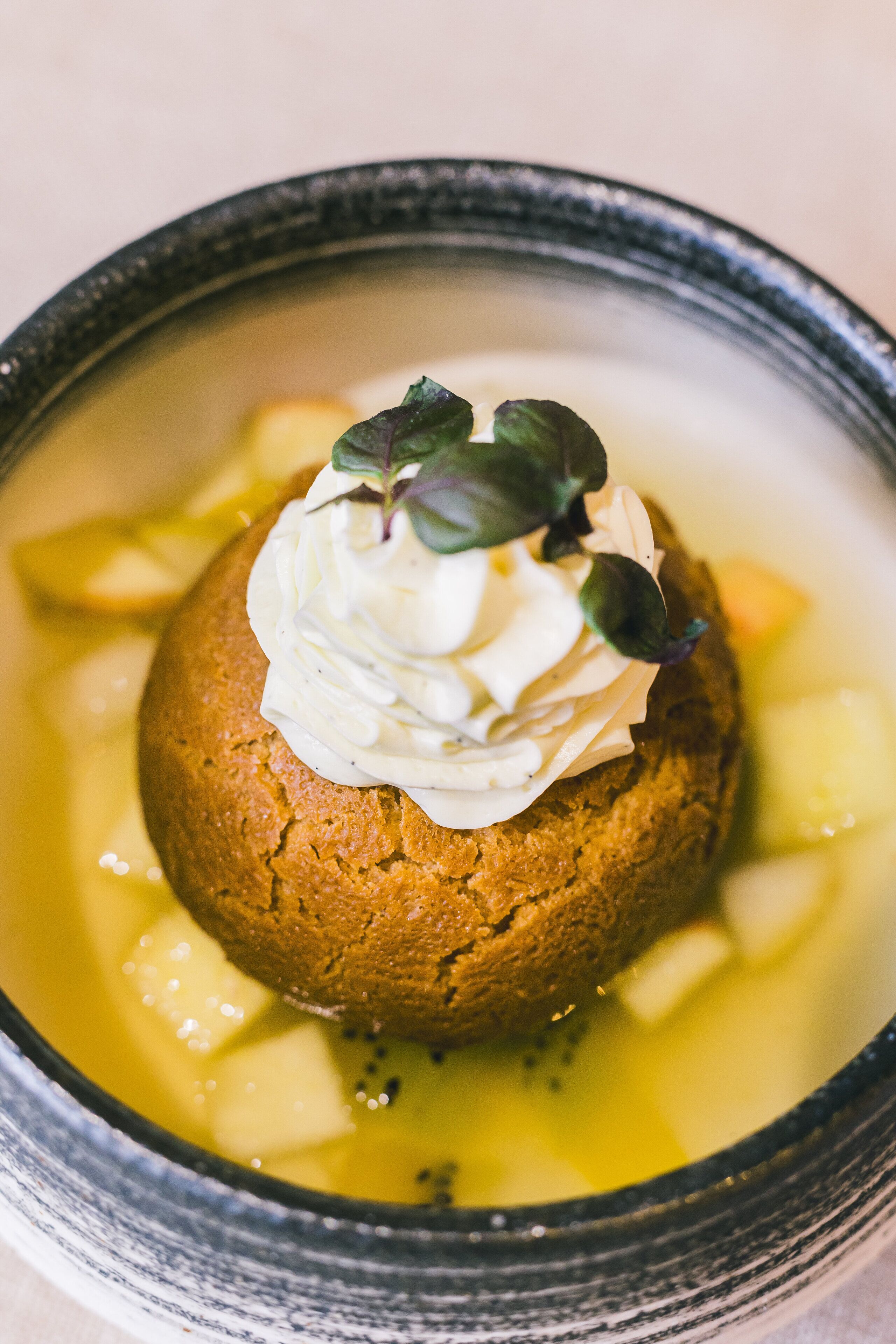 A dessert in a bowl with a dollop of cream and a leaf garnish.
