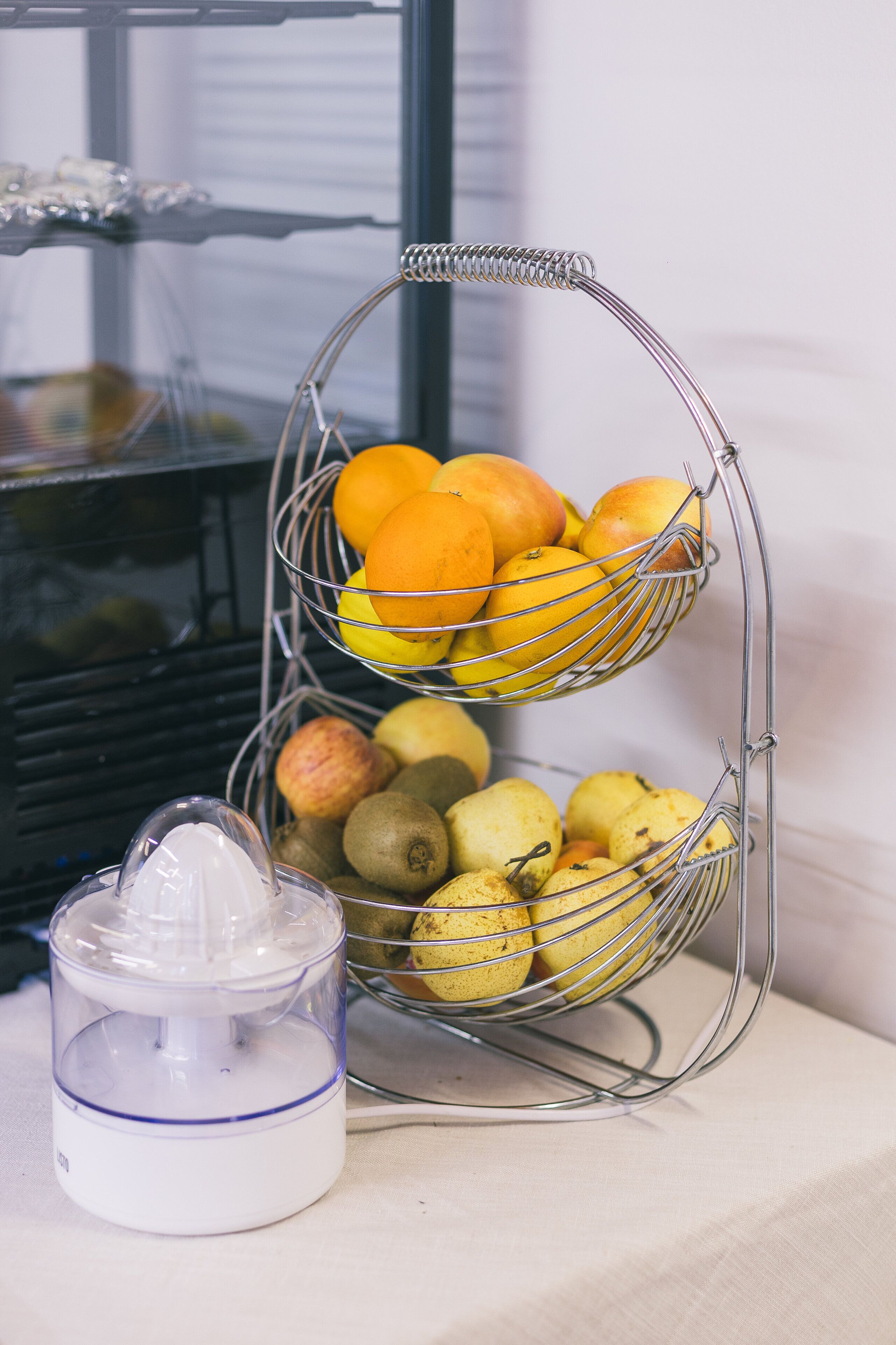 A fruit stand with oranges and kiwis, and a juicer on a table.