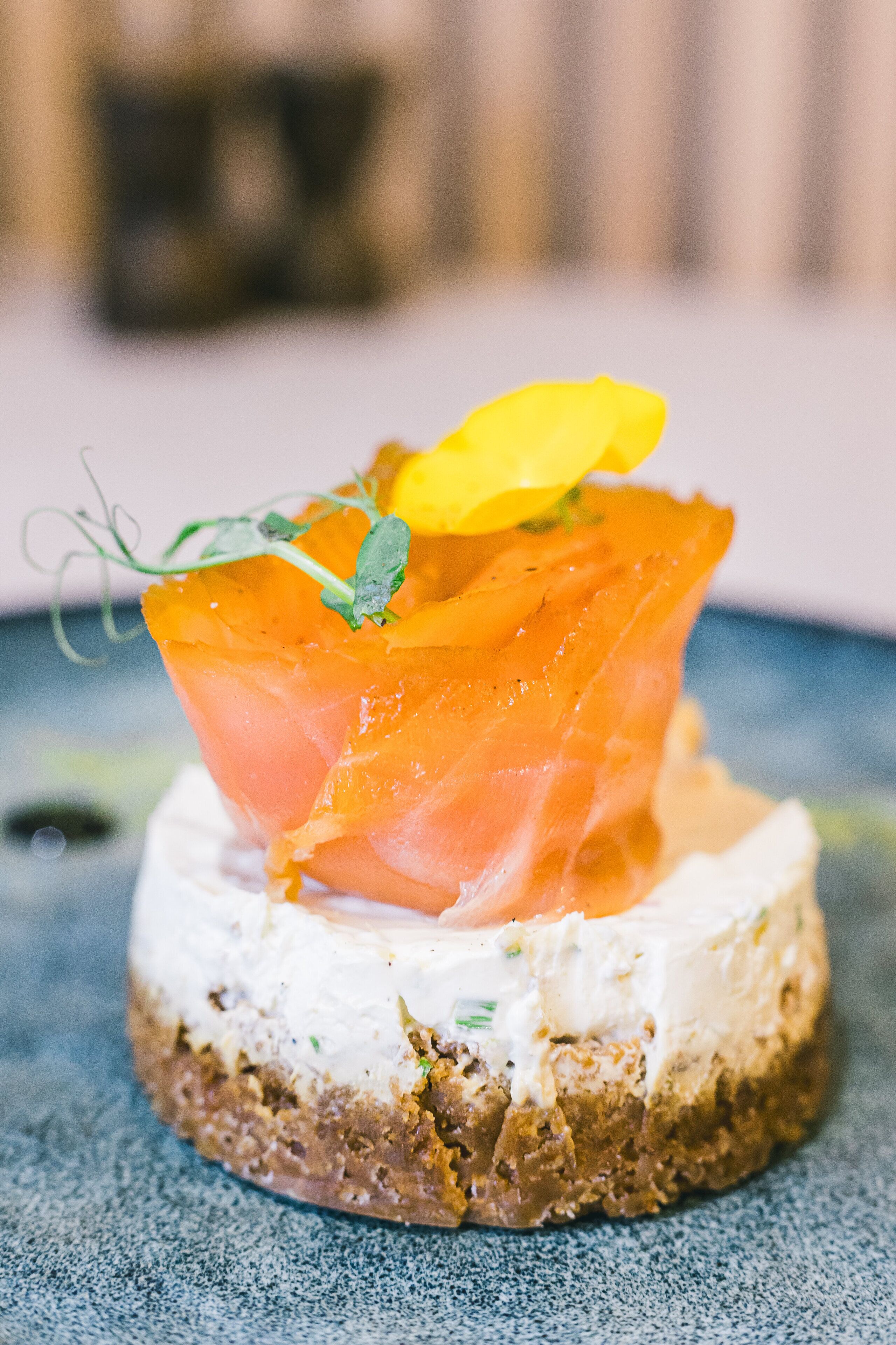 A round, multi-layered appetizer with smoked salmon, cream, and a yellow garnish on a round cracker base.