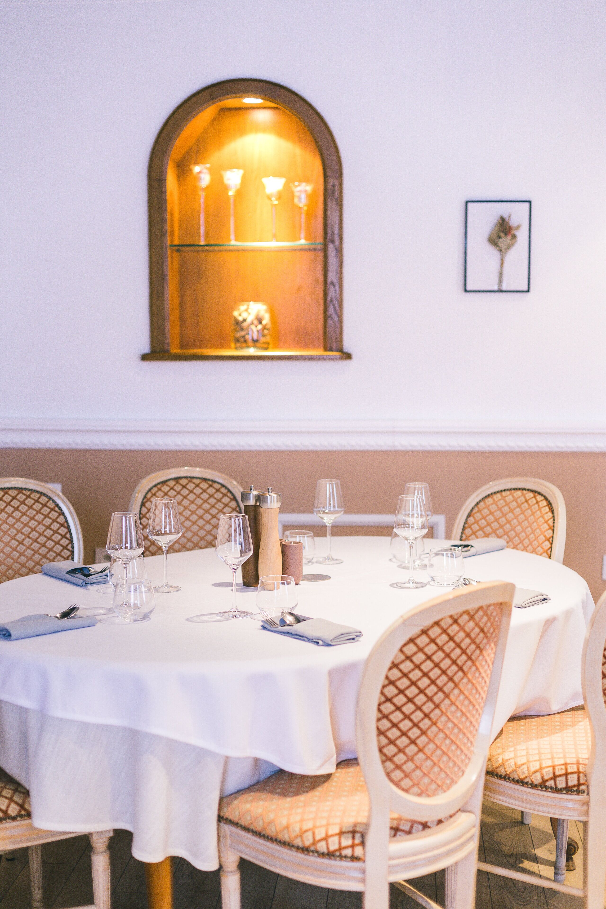 A dining table set with white tablecloth, surrounded by wicker chairs with cushioned seats, and a wall-mounted light fixture above.