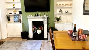 Un salon doté d’une cheminée, avec un téléviseur fixé au-dessus, et un coin repas comprenant une table et des chaises.