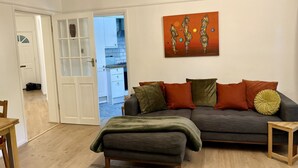 Un salon avec un canapé gris, des coussins verts et orange, une table basse en bois et un tableau accroché au mur.