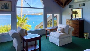 A room with a large arched window overlooking the sea, a wooden dresser, a white armchair, and a small table. - Luxury Waterfront Home on Harrington Sound in Smith's Parish (Flatts Village)