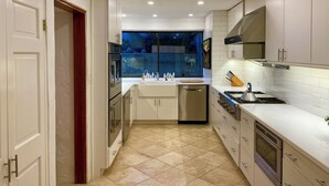 A modern kitchen with white cabinets, stainless steel appliances, and a tiled floor. - Luxury Waterfront Home on Harrington Sound in Smith's Parish (Flatts Village)