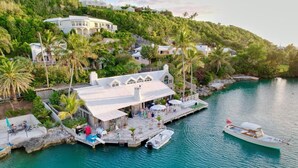 A coastal property with a dock, a boat, and a building with a white roof. - Luxury Waterfront Home on Harrington Sound in Smith's Parish (Flatts Village)