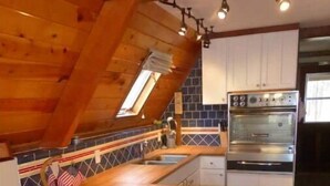 Une cuisine avec un plafond en bois, un four encastré et un petit îlot central doté d’un évier.