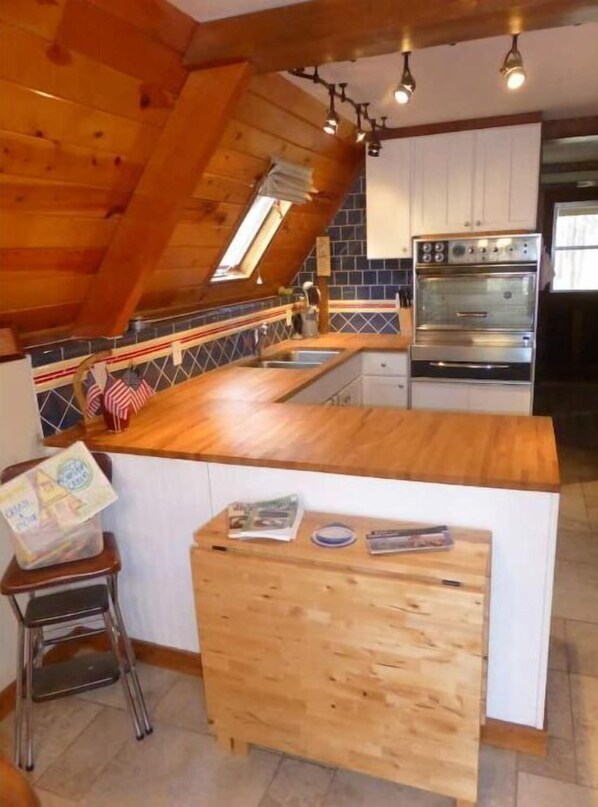 A kitchen with a wooden ceiling, a built-in oven, and a small island with a sink.