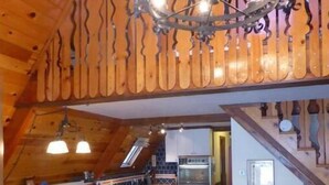 Une cuisine chaleureuse avec des poutres apparentes en bois au plafond, un îlot central et un coin repas avec une table et des chaises rouges.