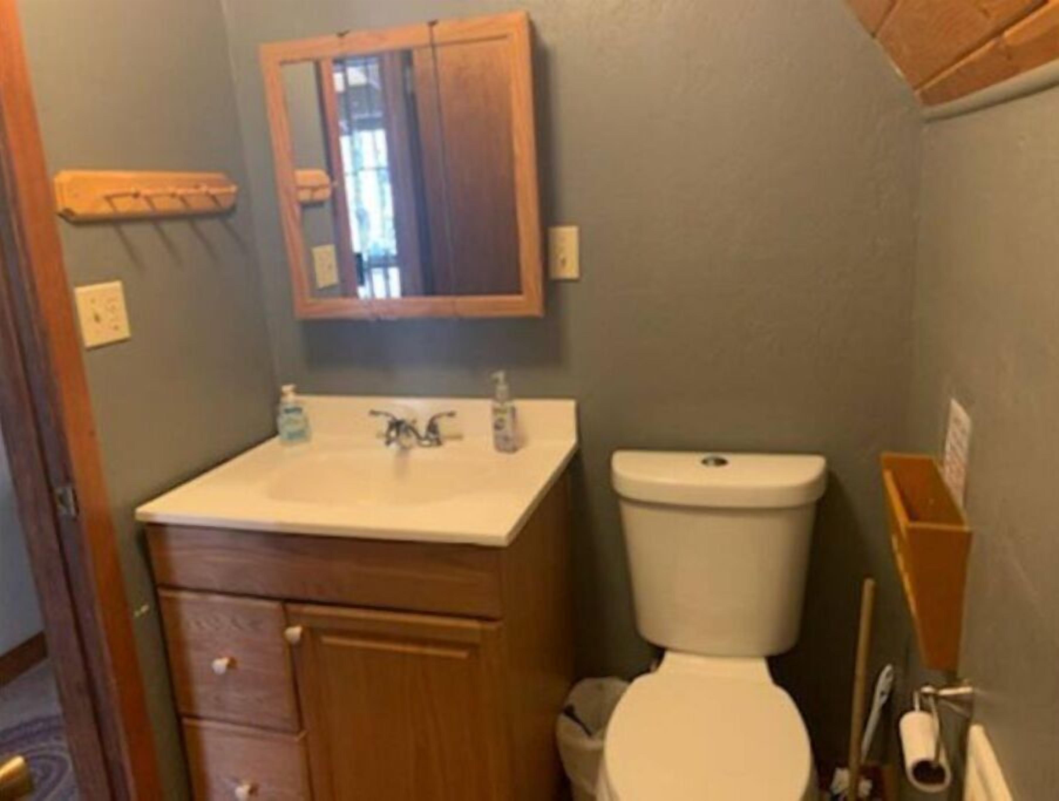 A bathroom with a wooden vanity, a sink, a mirror, and a toilet.