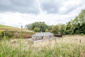 Ein Steinhhaus mit geneigtem Dach, umgeben von grünen Wiesen und Bäumen.