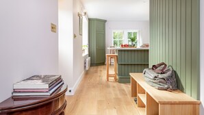 A narrow hallway with a wooden bench, a green door, and a window with a view of greenery.