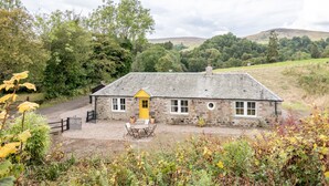 A stone house with a yellow door, a gravel driveway, and a small outdoor seating area.