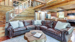 Interno di una baita in legno con un divano modulare in pelle, un tavolino in legno e una scala che conduce a un piano superiore.