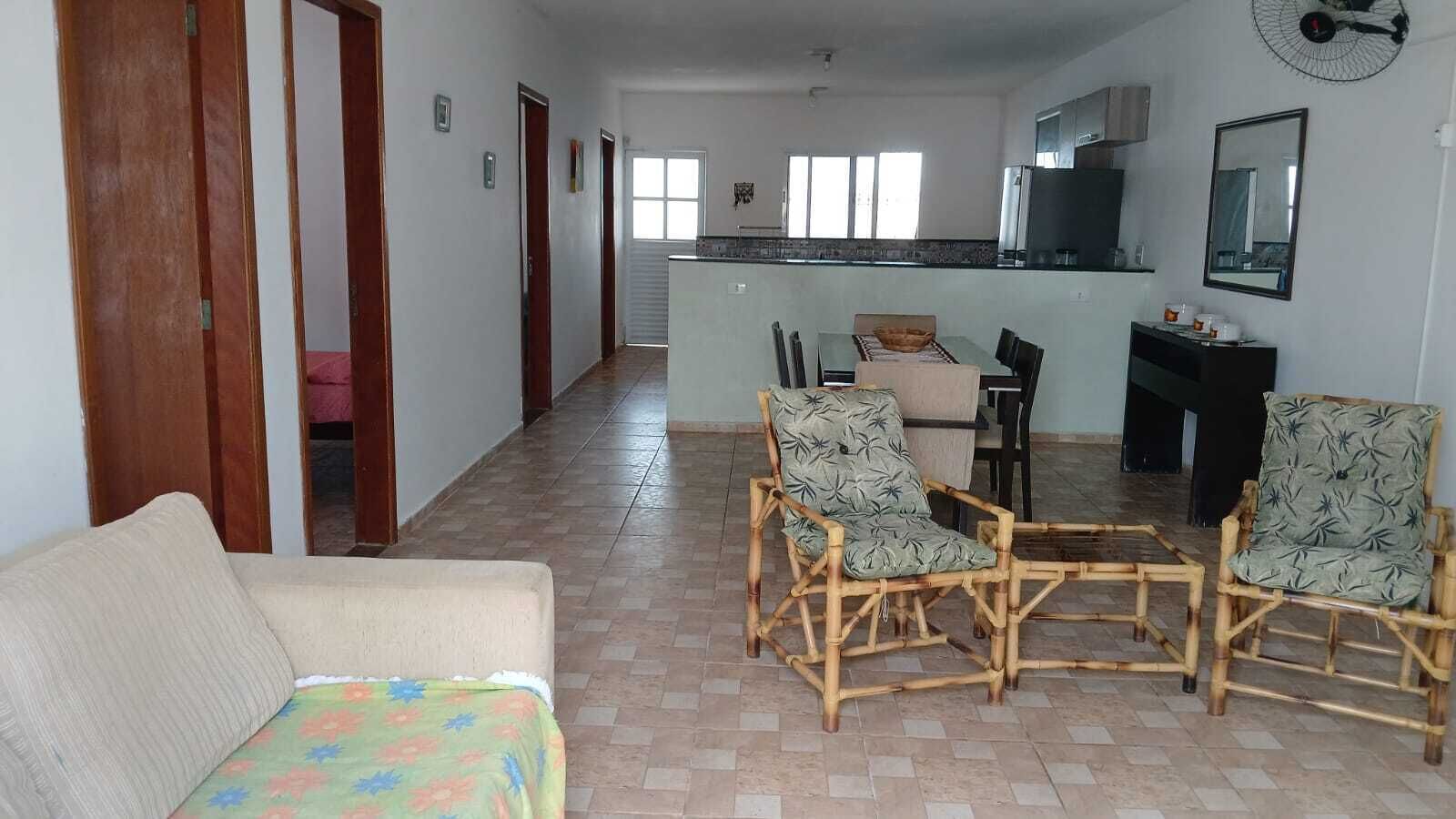 Una sala de estar con un sofá, dos sillas de bambú, una mesa de comedor y una cocina al fondo.