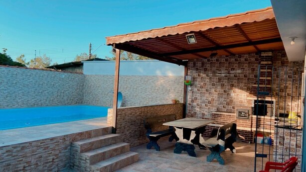 A pool area with a covered patio, outdoor seating, and a brick wall. - House with pool and huge backyard for children!!! (Peruíbe)