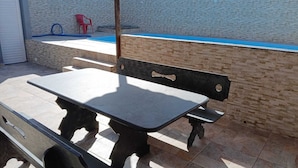 An outdoor patio with a table and benches, a pool, and a brick wall. - House with pool and huge backyard for children!!! (Peruíbe)