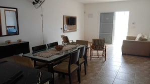 A dining area with a table, chairs, a TV mounted on the wall, and a sliding door leading to another room. - House with pool and huge backyard for children!!! (Peruíbe)