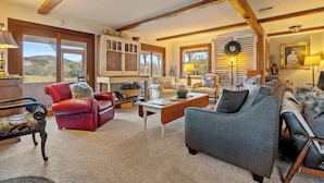 A cozy living room with a red leather chair, a grey sofa, and a wooden coffee table. There is a window with a view of the outdoors. - Hot Tub + Fire Pit | Vineyard Near Templeton + Paso | Vineyard Retreat (Templeton)