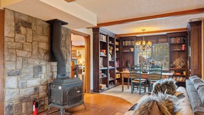 A cozy living room with a stone wall, a fireplace, a bookshelf, and a comfortable sofa. - Hot Tub + Fire Pit | Vineyard Near Templeton + Paso | Vineyard Retreat (Templeton)