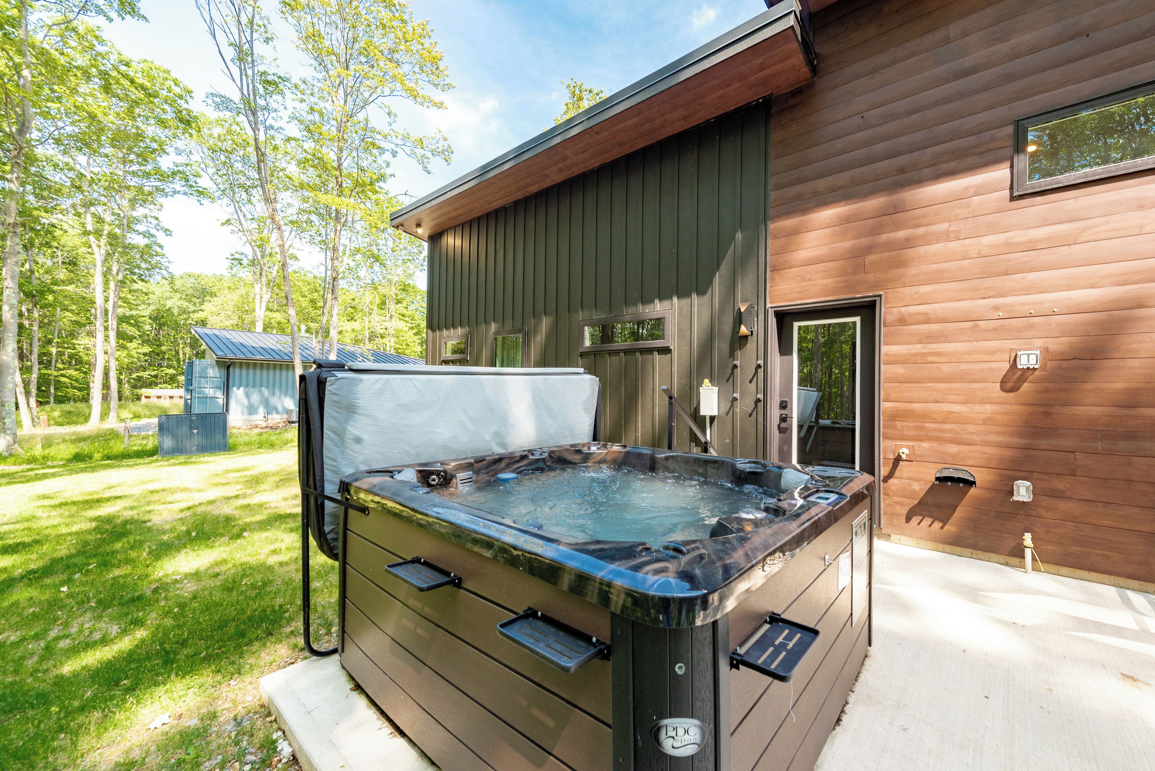A hot tub in front of a wooden cabin with a metal roof, surrounded by trees.