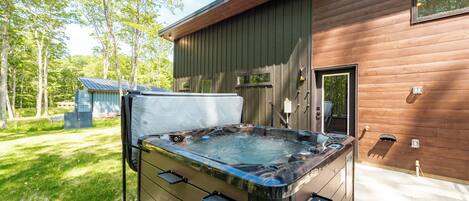 A hot tub in front of a wooden cabin with a metal roof, surrounded by trees.