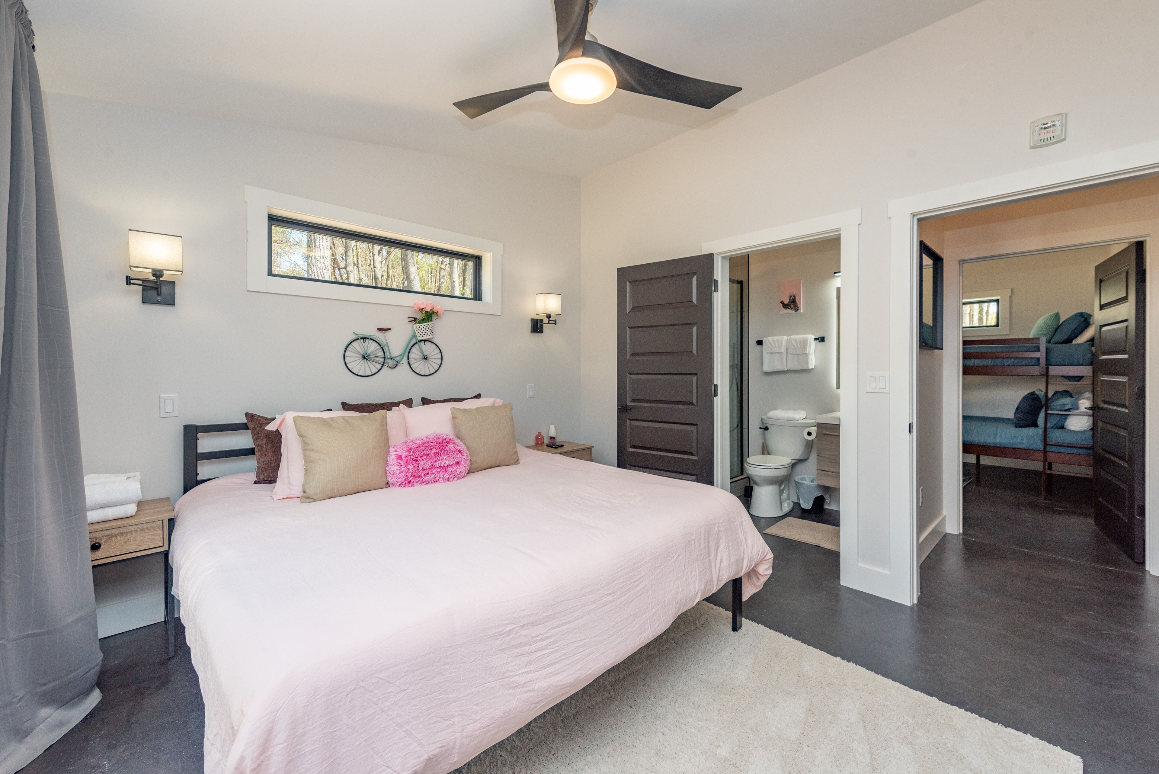 Un dormitorio con una cama grande, un ventilador de techo, una ventana y una bicicleta decorativa en la pared.