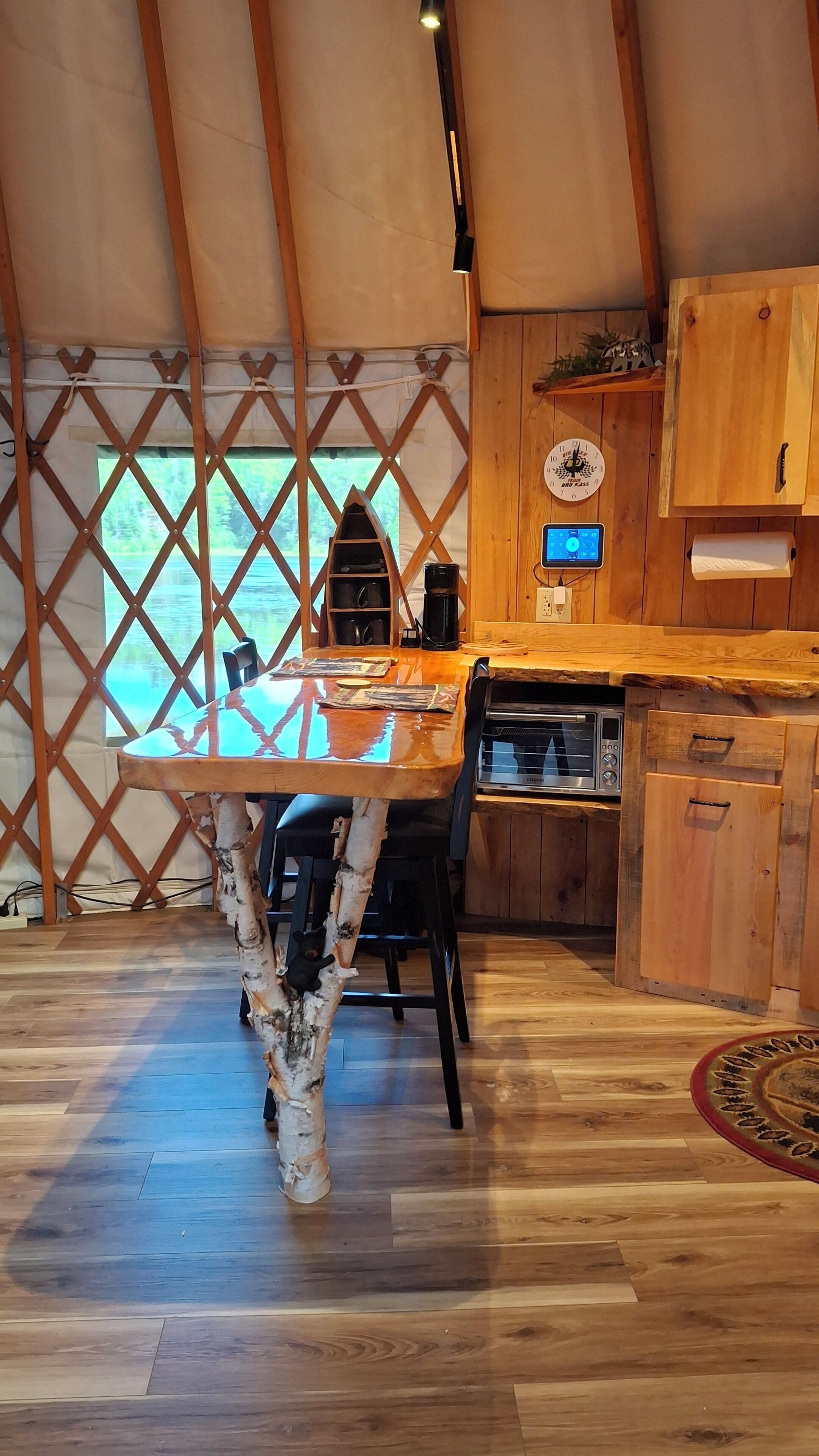 Un interior de madera con una mesa de comedor, sillas, una cafetera y un reloj en la pared.
