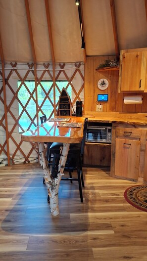 A wooden interior with a dining table, chairs, a coffee machine, and a clock on the wall.