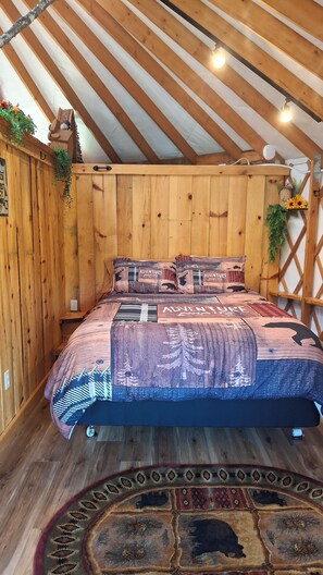 Une pièce en bois avec un lit, une étagère fixée au mur et une plante suspendue.