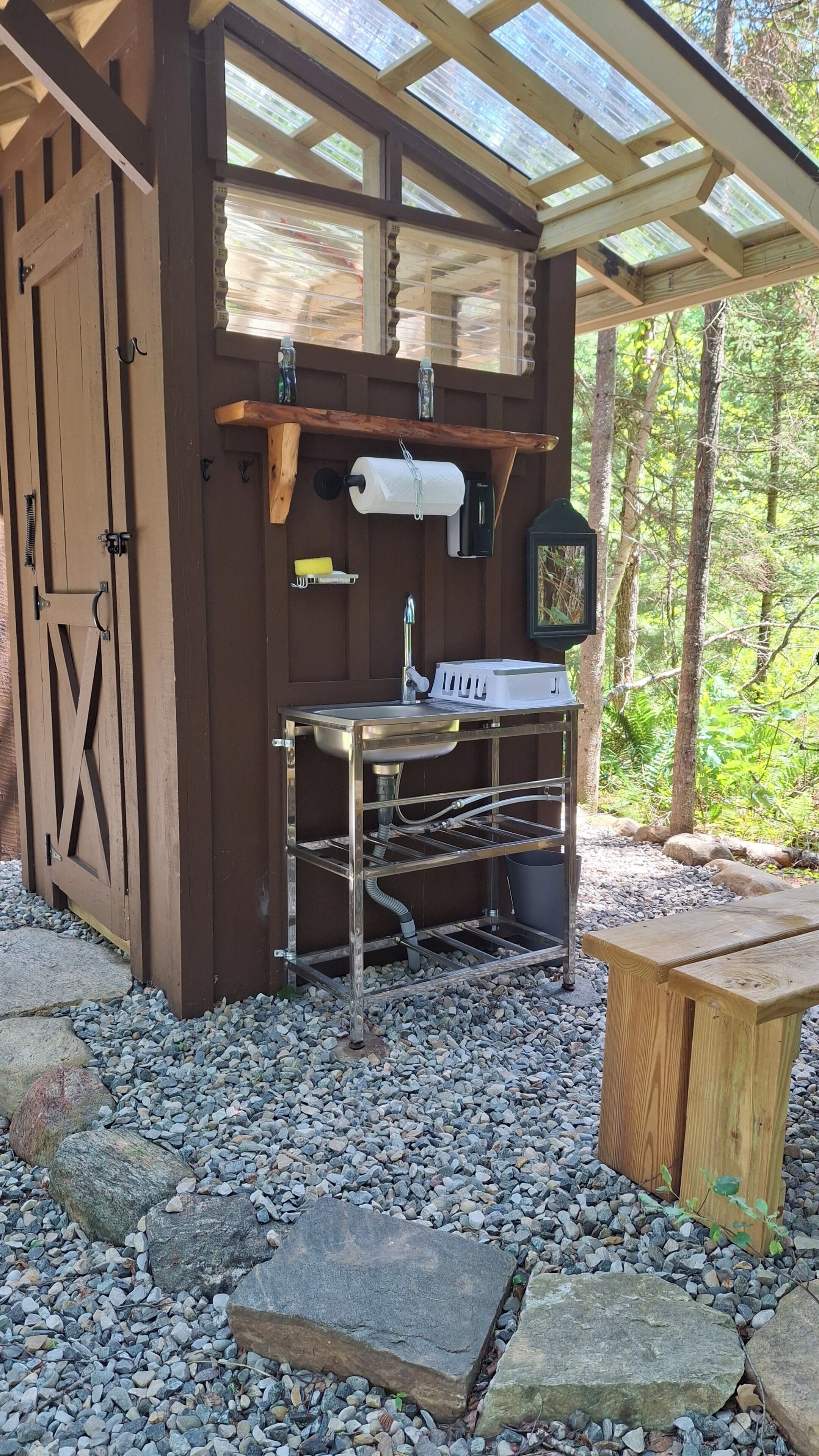 A rustic outdoor kitchen with a wooden structure, a sink, and a hanging faucet.