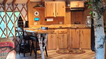 Interior espacioso de una yurta, con una zona de comedor de madera, una cocina con armarios y un abedul.