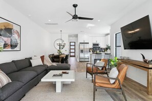 A modern living room with a sofa, coffee table, and chairs, a dining area with a table and chairs, and a kitchen with appliances.