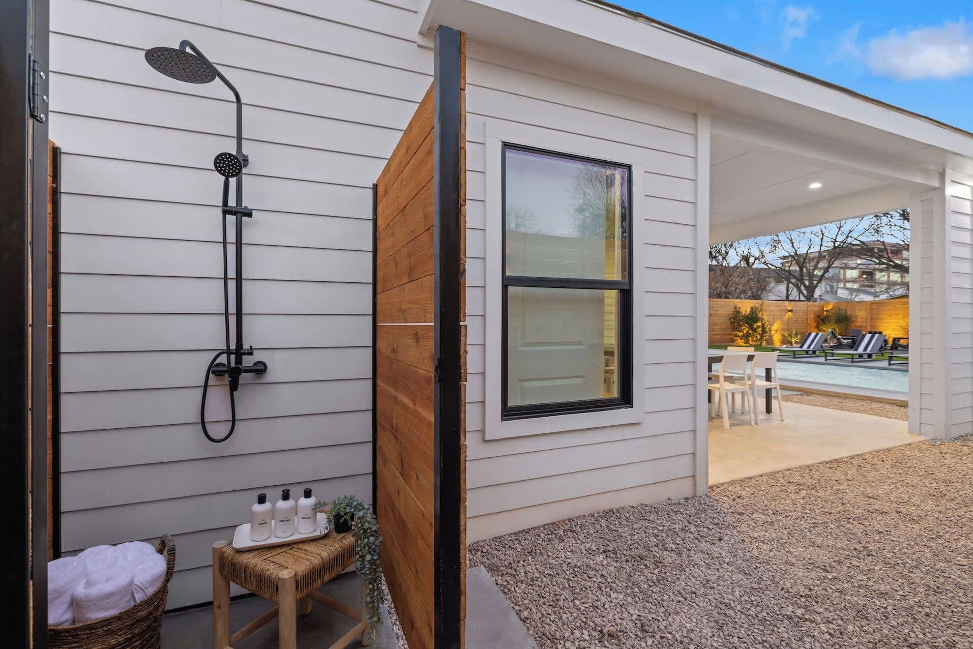 A modern house with a built-in shower, a large window, and a pool area visible through an open door.