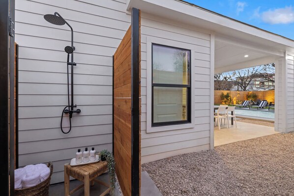 A modern house with a built-in shower, a large window, and a pool area visible through an open door.