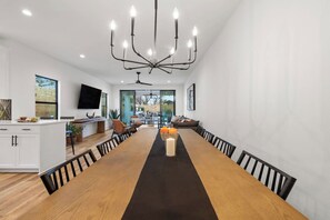 A modern dining area with a long wooden table, black chairs, and a chandelier.