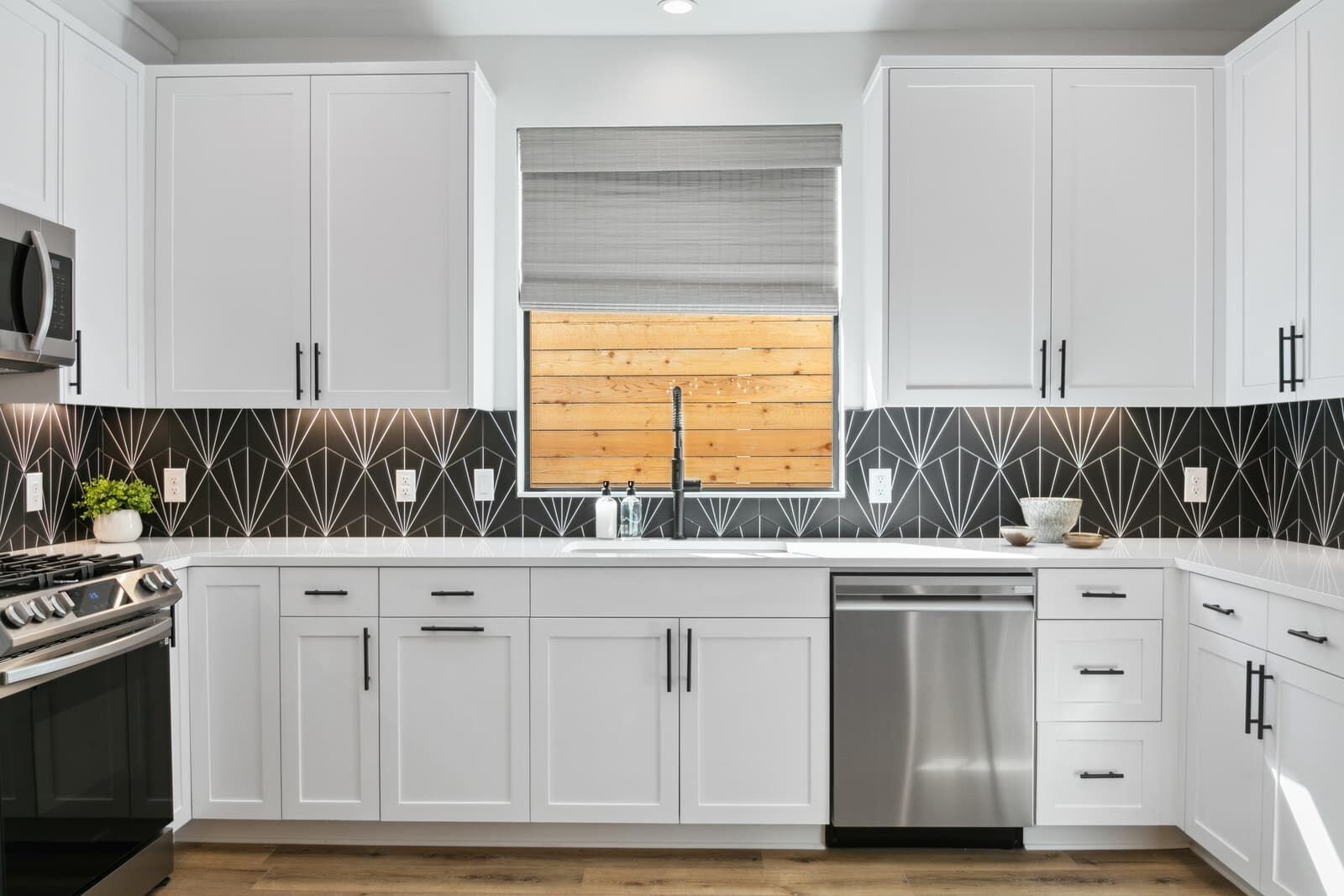 A modern kitchen with white cabinetry, a stainless steel dishwasher, and a black and white patterned backsplash.