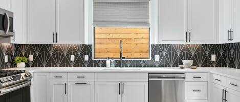 A modern kitchen with white cabinetry, a stainless steel dishwasher, and a black and white patterned backsplash.