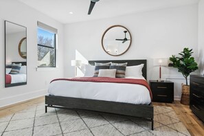 A modern bedroom with a bed, a round mirror, a ceiling fan, and a view of the outdoors.