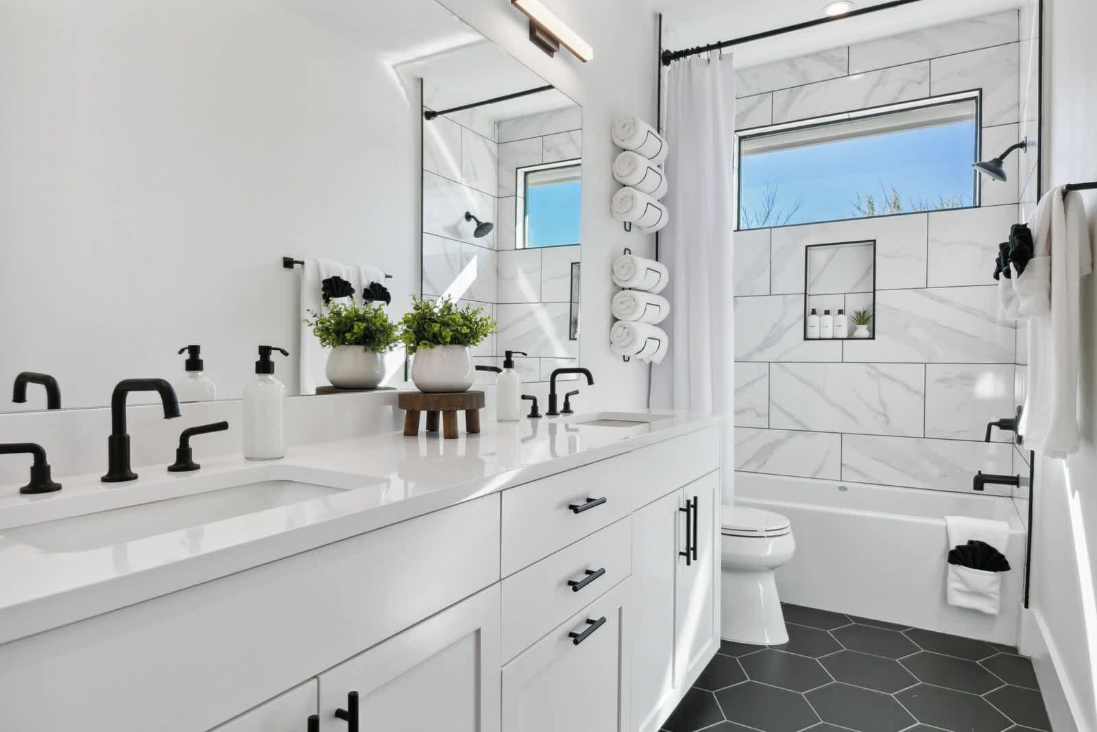 Een moderne badkamer met een grote spiegel, witte marmeren tegels, een badkuip en een douche.